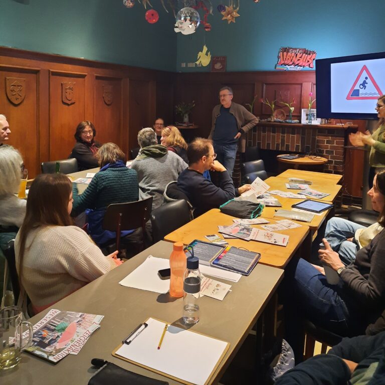 Das Foto zeigt Menschen, die an Tischen zeichnen und dem Cartoonisten Phil Hubbe zuhören.